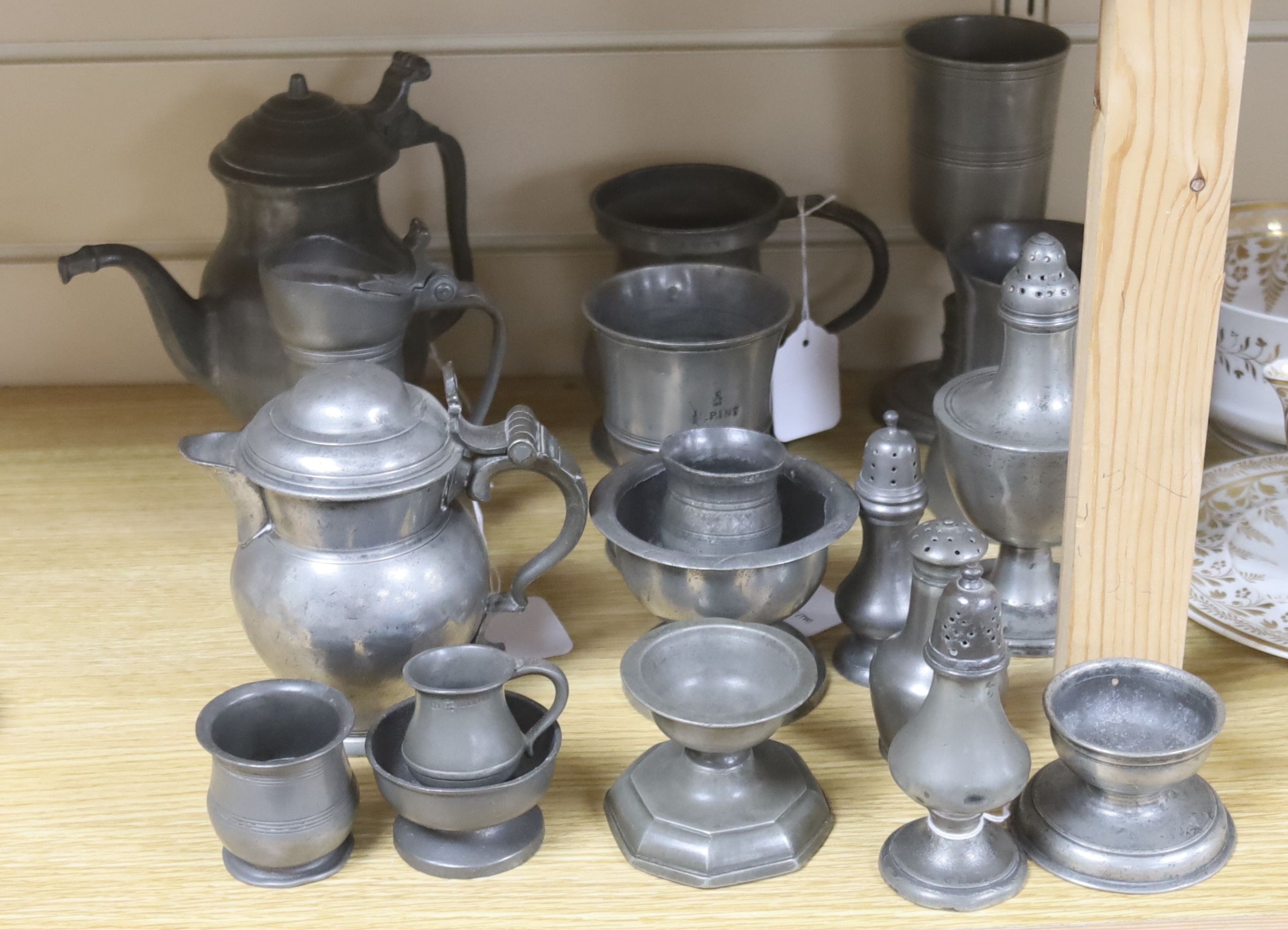 Eighteen items of 18th and 19th century pewter, including lidded jugs, measures, goblets, salt and pepper pots and a chocolate pot